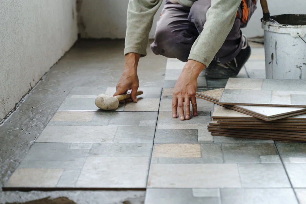 Artisan carreleur à genoux installant un revêtement de sol dans un espace intérieur