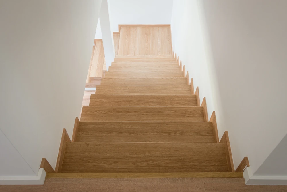 Escalier en bois clair avec marches et contremarches dans un intérieur moderne aux murs blancs