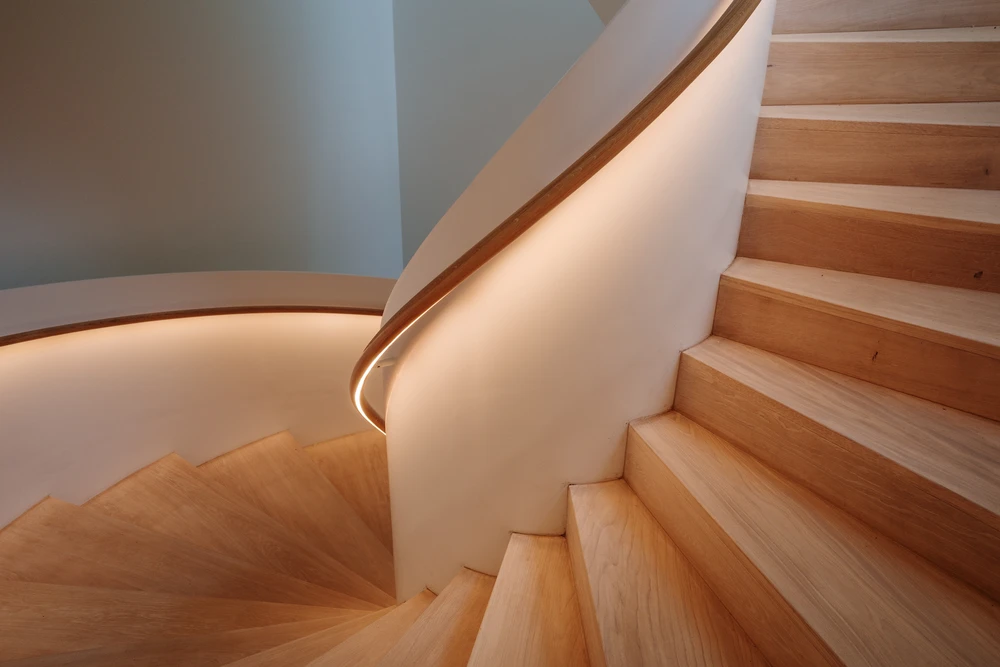 Escalier hélicoïdal moderne en bois clair avec main courante intégrée dans une architecture contemporaine aux murs blanc cassé