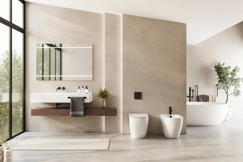 Un chantier de rénovation d'intérieur en cours : deux ou trois artisans qualifiés d'une même équipe travaillant en coordination dans une salle de bain moderne en transformation. L'un installe une robinetterie tandis qu'un autre effectue des finitions de carrelage ou de peinture à proximité. L'image doit montrer clairement une collaboration interne, une cohérence de chantier et l'absence de segmentation des tâches. Les artisans doivent porter des tenues professionnelles uniformisées (salopette ou uniforme de la même marque/couleur) pour souligner l'unité de l'équipe CNR. L'arrière-plan doit montrer un chantier bien organisé avec des outils et des matériaux professionnels visibles, reflétant un suivi qualitatif et coordonné du projet du début à la fin.