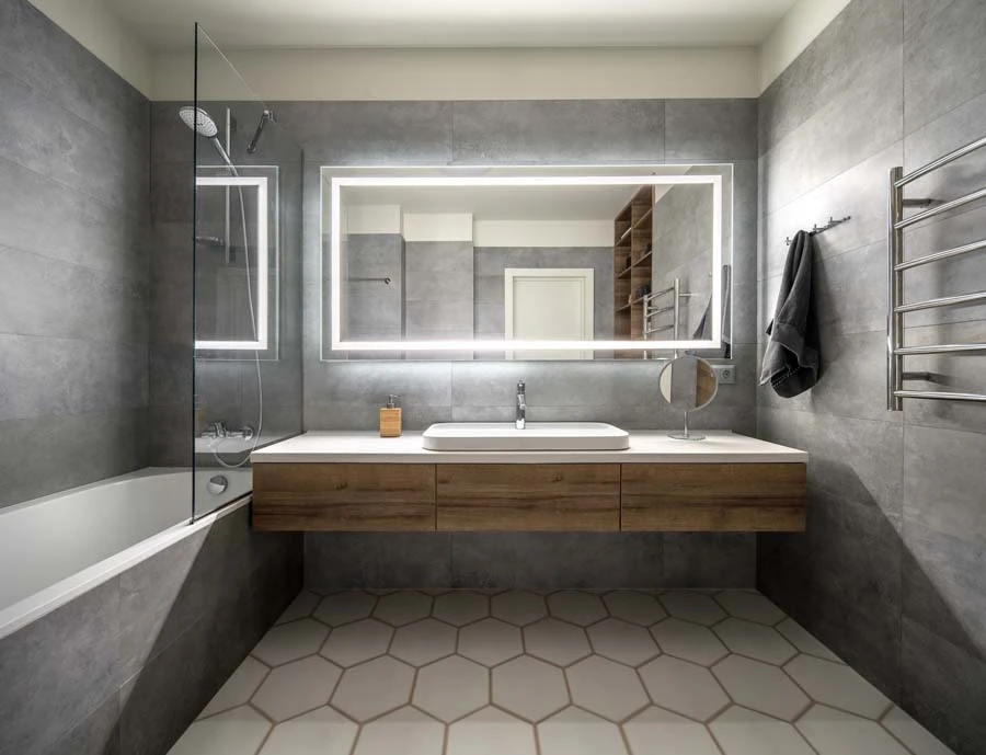 Deux artisans en combinaisons noires et t-shirts orange installent un meuble dans une salle de bain moderne aux murs en marbre blanc
