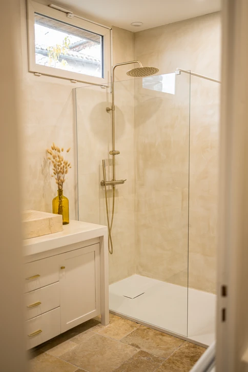 Un chantier de rénovation d'intérieur en cours : deux ou trois artisans qualifiés d'une même équipe travaillant en coordination dans une salle de bain moderne en transformation. L'un installe une robinetterie tandis qu'un autre effectue des finitions de carrelage ou de peinture à proximité. L'image doit montrer clairement une collaboration interne, une cohérence de chantier et l'absence de segmentation des tâches. Les artisans doivent porter des tenues professionnelles uniformisées (salopette ou uniforme de la même marque/couleur) pour souligner l'unité de l'équipe CNR. L'arrière-plan doit montrer un chantier bien organisé avec des outils et des matériaux professionnels visibles, reflétant un suivi qualitatif et coordonné du projet du début à la fin.